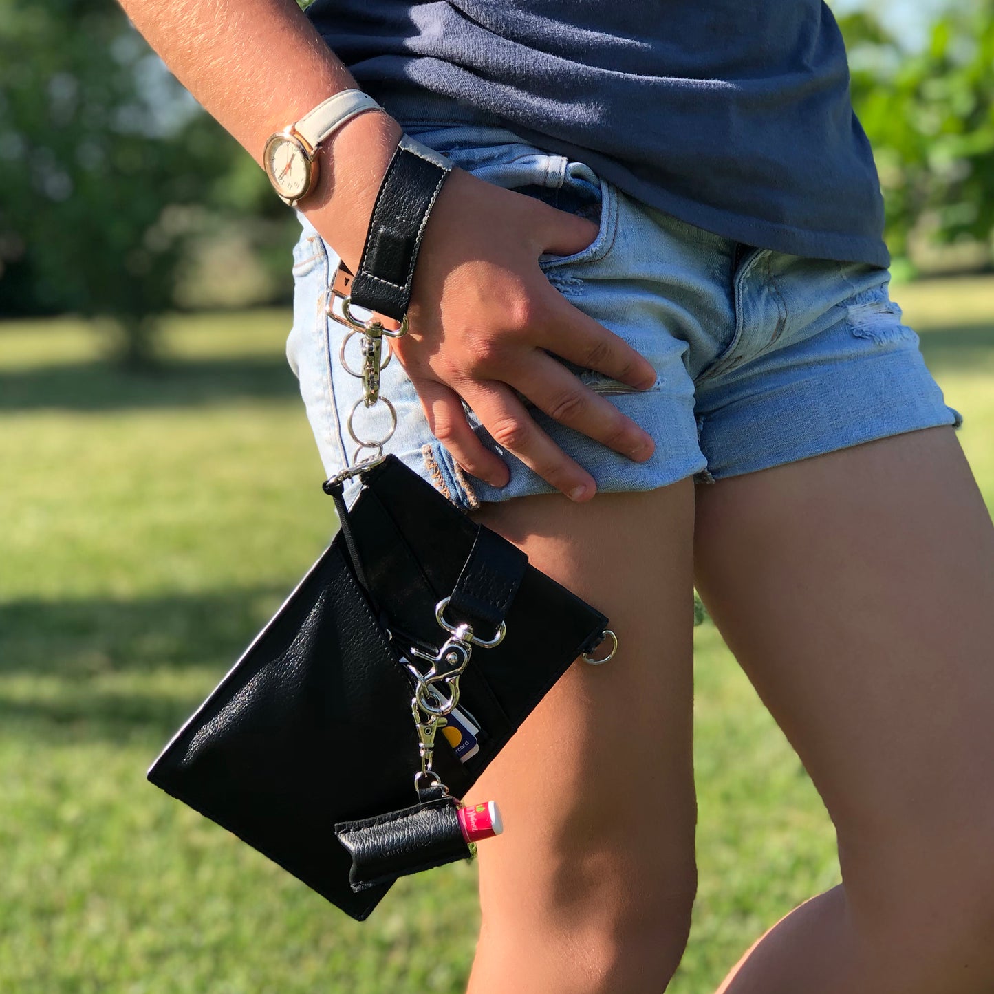 A person with a black vegan leather phone pouch with a black vegan leather magnetic wristlet key chain and a black removable three pocket wallet and black lip balm holder set.